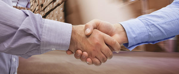Close up of two men engaged in a handshake in a warehouse. Image used to represent Trading Partners.